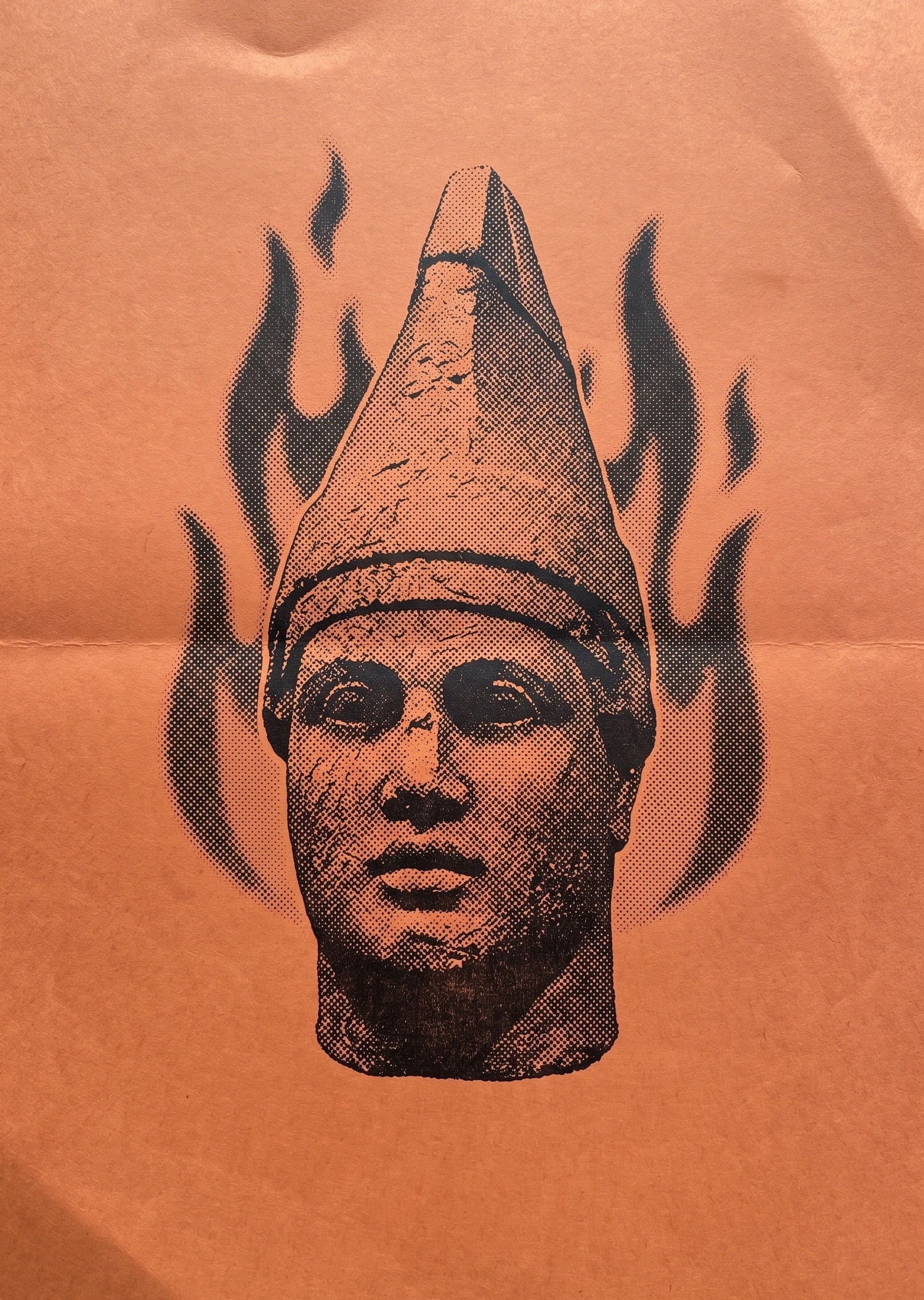 Halftone print of a stone head in a pointed cap above flames, on orange paper